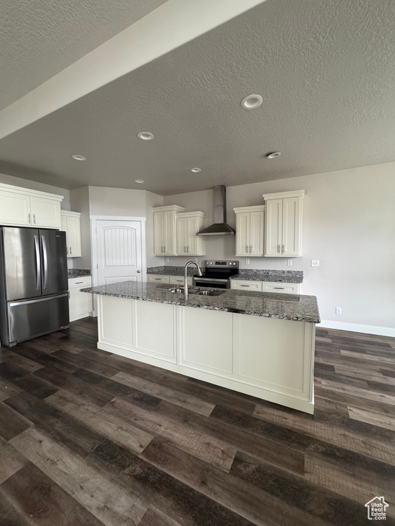 Kitchen featuring dark wood-type flooring, wall chimney range hood, dark stone countertops, and appliances with stainless steel finishes
