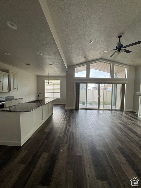 Unfurnished living room with a ceiling fan, dark wood-style floors, baseboards, lofted ceiling, and a sink