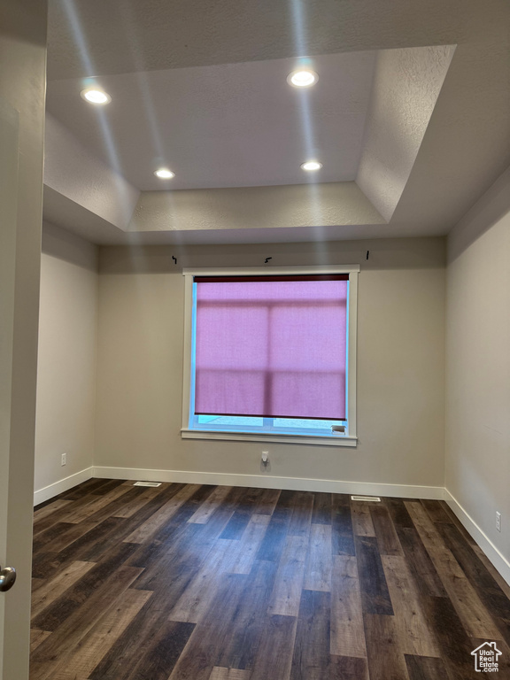 Spare room featuring a tray ceiling, baseboards, and wood finished floors