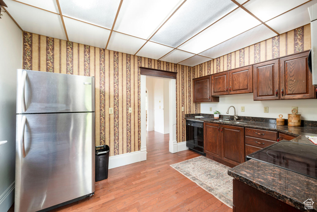 Kitchen with freestanding refrigerator, dishwasher, a sink, wallpapered walls, and baseboards
