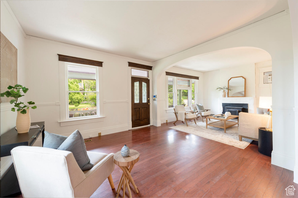 Living room featuring arched walkways, wood finished floors, a glass covered fireplace, baseboards, and ornamental molding