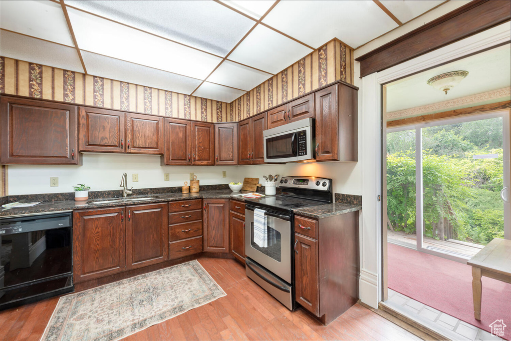 Kitchen with appliances with stainless steel finishes, a sink, light wood-style floors, and dark stone counters