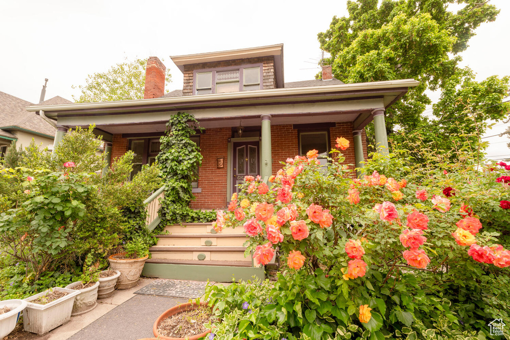View of front of house featuring a chimney, covered porch, and brick siding