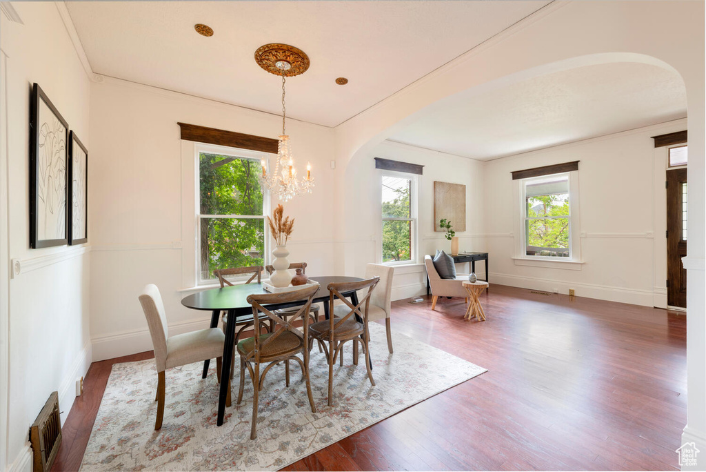 Dining area with wood finished floors, arched walkways, a chandelier, and baseboards