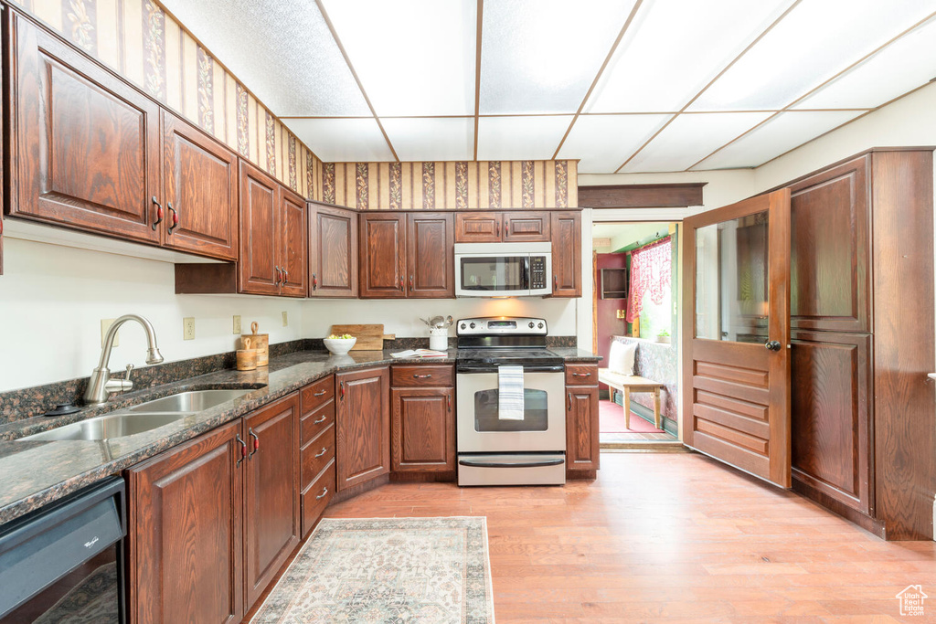 Kitchen with stainless steel appliances, a sink, light wood-style floors, dark stone countertops, and a drop ceiling