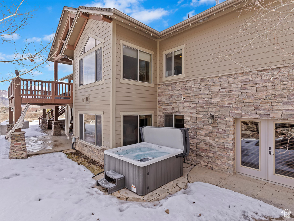View of snowy exterior featuring stone siding, a patio, a wooden deck, stairs, and a hot tub