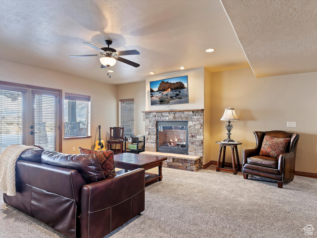 Living area with baseboards, carpet flooring, a stone fireplace, a textured ceiling, and a ceiling fan