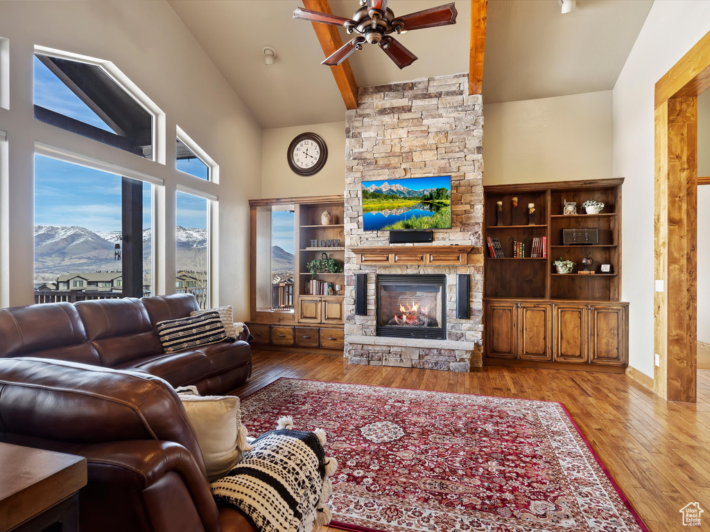 Living room featuring wood finished floors, a ceiling fan, high vaulted ceiling, beam ceiling, and a fireplace