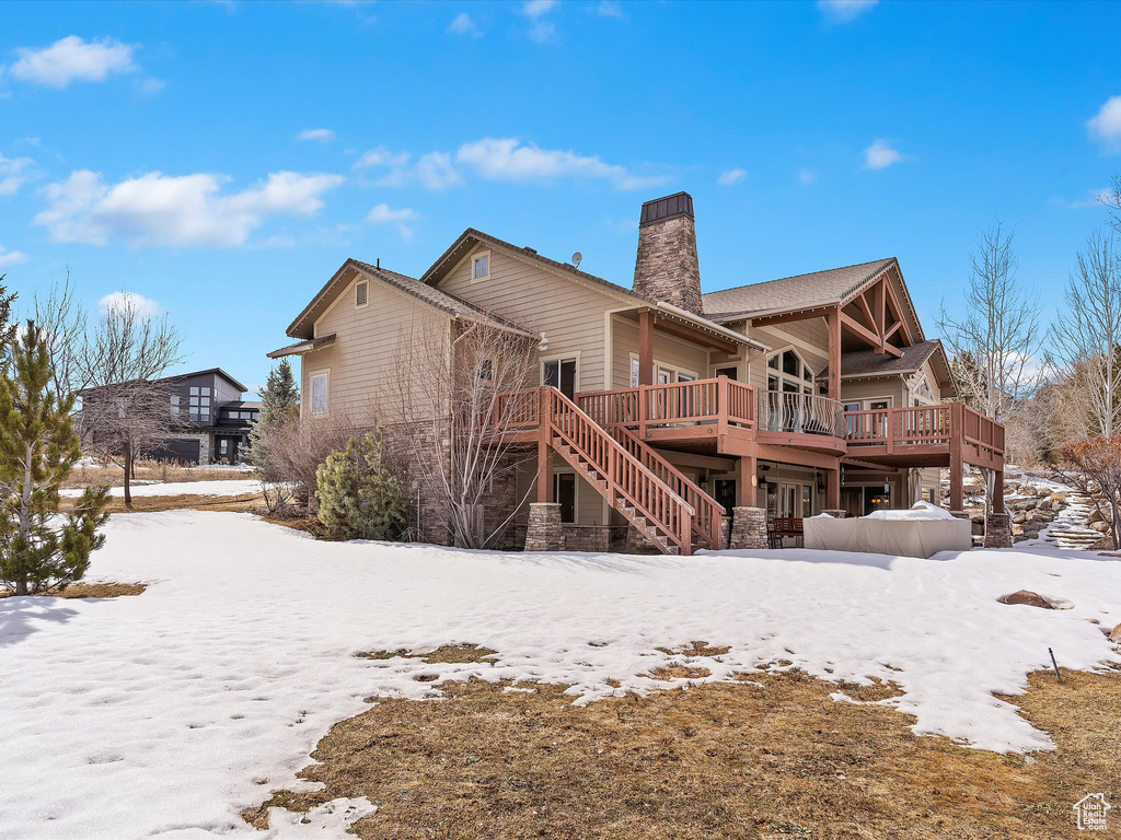 Snow covered house with stairway, a chimney, and a wooden deck