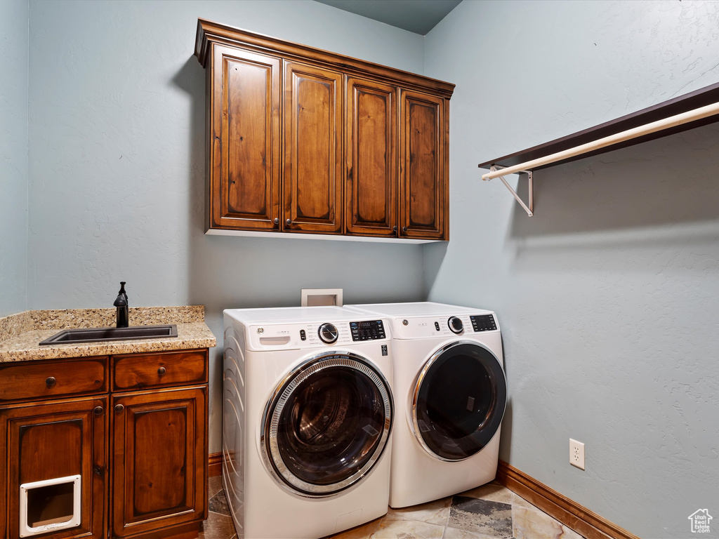 Clothes washing area with cabinet space, washer and dryer, baseboards, and a sink