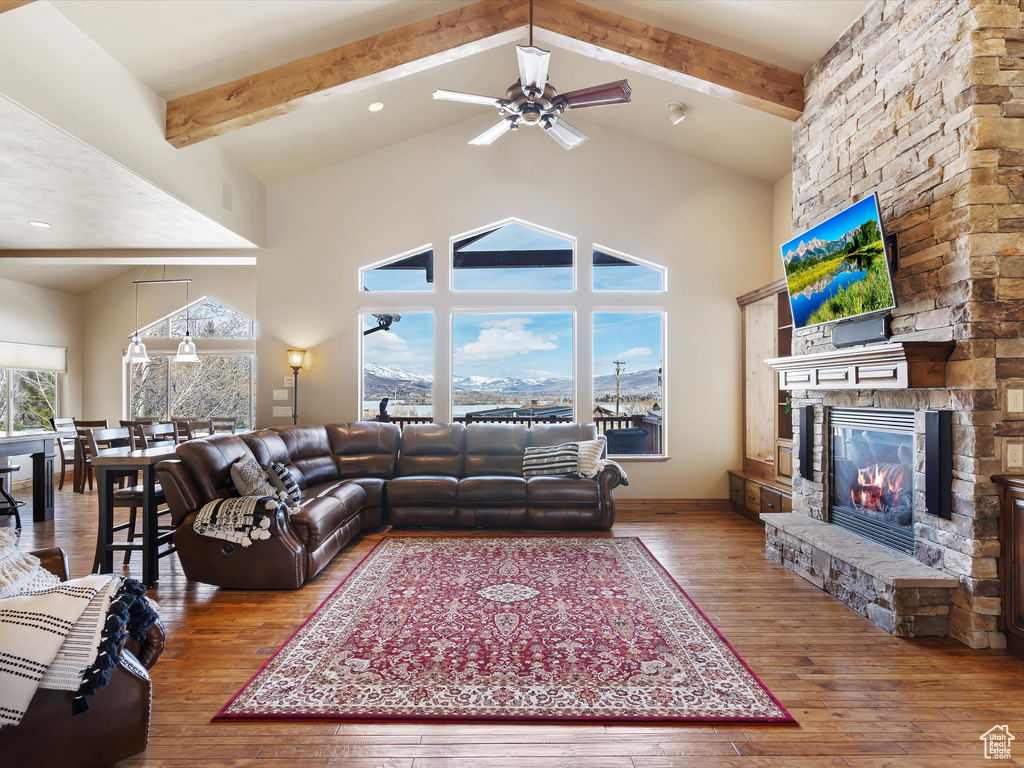 Living room with a stone fireplace, beamed ceiling, high vaulted ceiling, and wood-type flooring