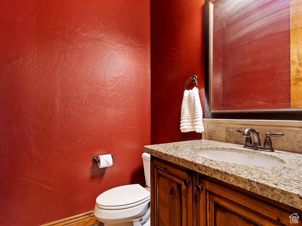 Half bathroom featuring toilet, vanity, and a textured wall