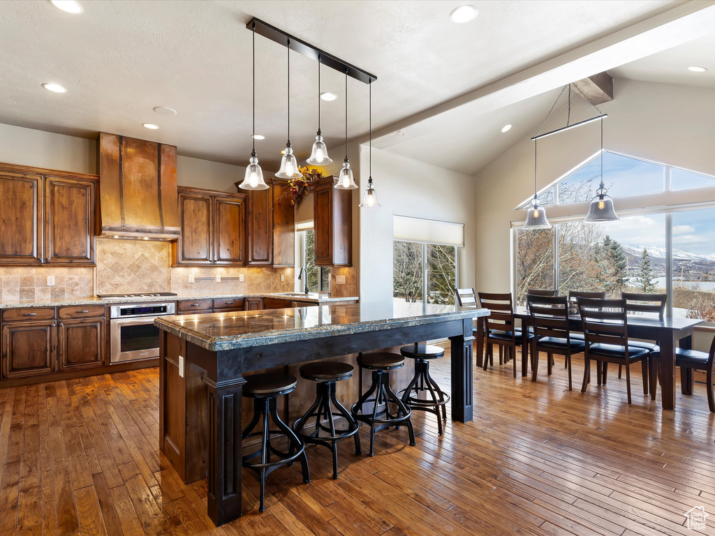 Kitchen with dark wood finished floors, custom exhaust hood, backsplash, and stainless steel appliances