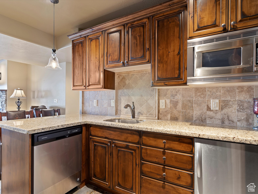 Kitchen with a sink, tasteful backsplash, appliances with stainless steel finishes, light stone countertops, and hanging light fixtures