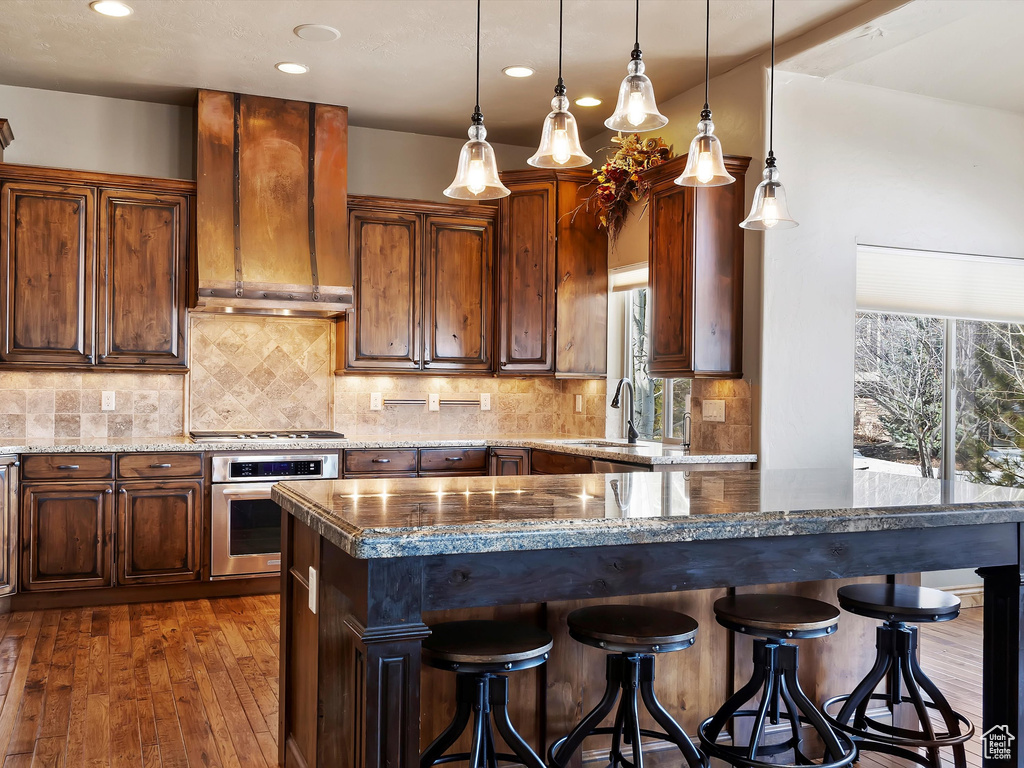 Kitchen with range hood, a breakfast bar area, a sink, appliances with stainless steel finishes, and backsplash