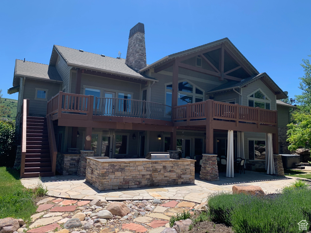 Rear view of property featuring stone siding, a chimney, stairway, a deck, and a patio area