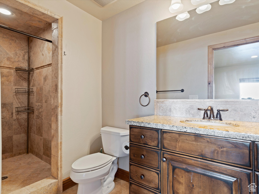 Bathroom with tiled shower, toilet, vanity, and baseboards