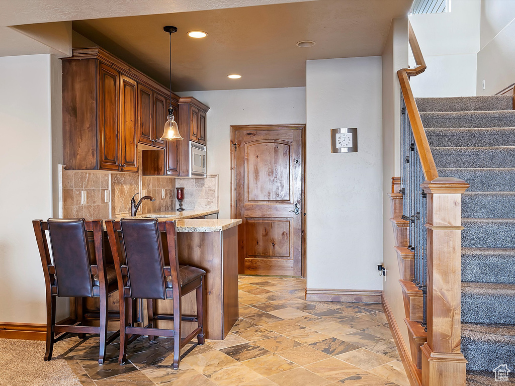 Kitchen with light stone counters, stainless steel microwave, backsplash, a peninsula, and a breakfast bar area