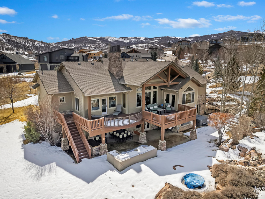 Snow covered back of property with stairway, a deck with mountain view, a residential view, and roof with shingles