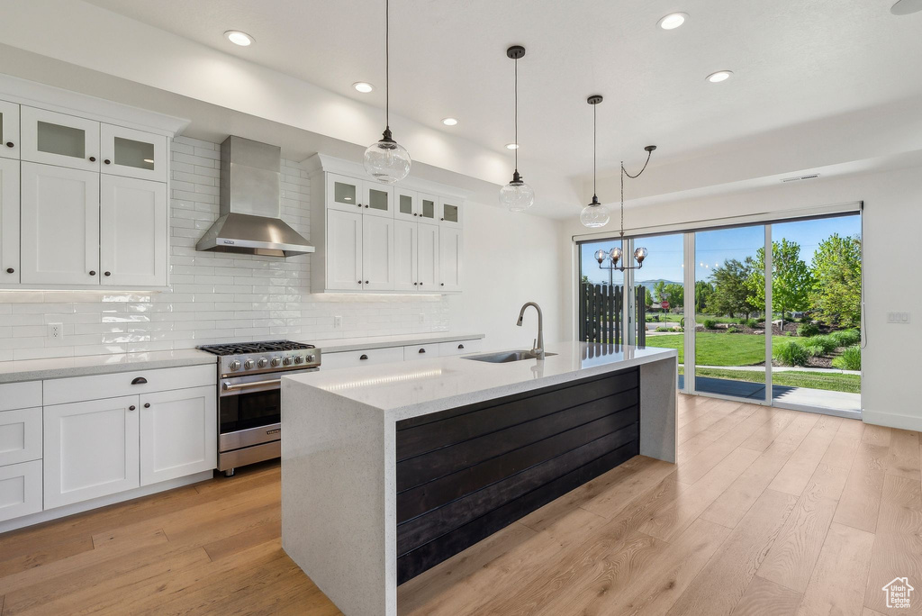 Kitchen featuring high end stainless steel range, wall chimney exhaust hood, a sink, tasteful backsplash, and light wood-style floors