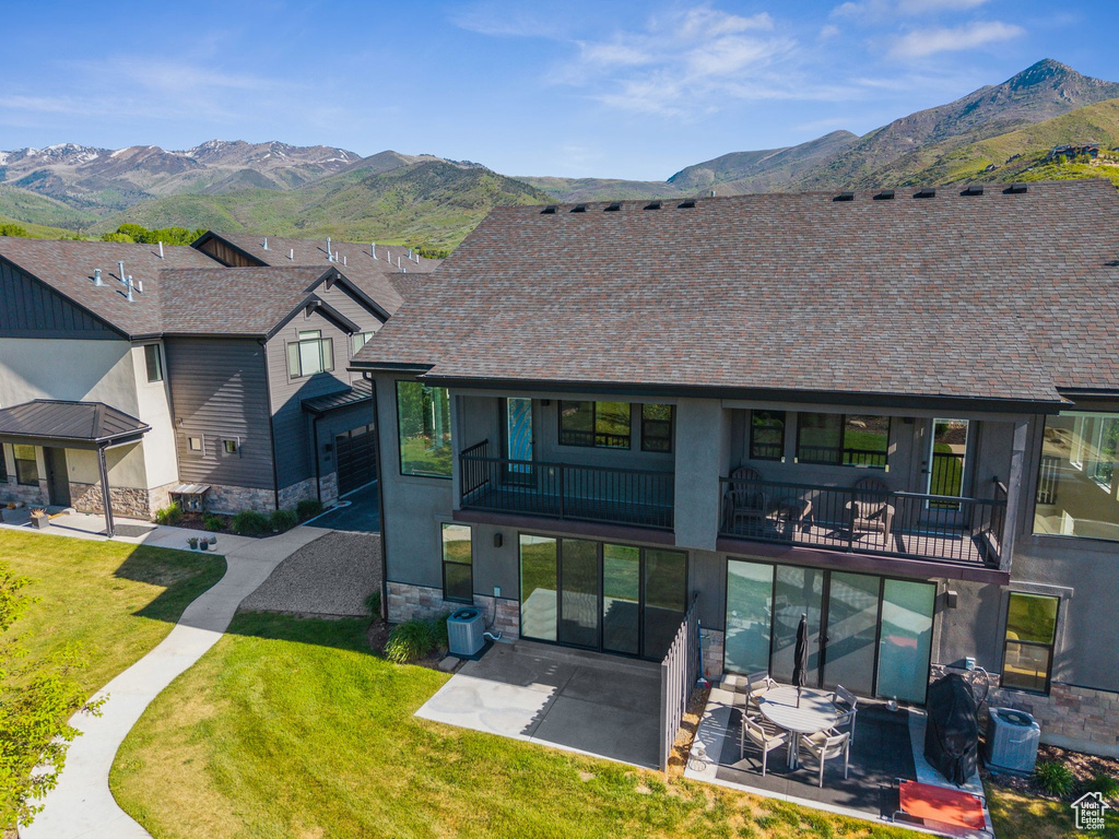 View of front of home with a balcony, a mountain view, a patio area, and stone siding