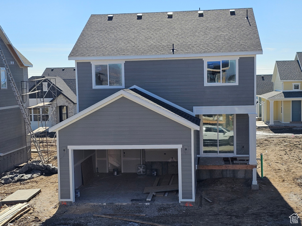 Back of house featuring a garage, driveway, and a shingled roof