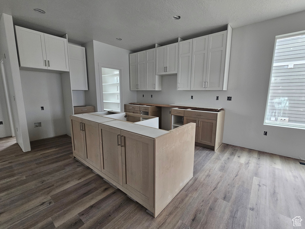 Kitchen with white cabinetry, a kitchen island, wood finished floors, and a textured ceiling