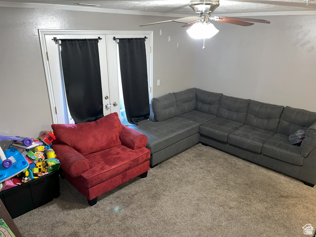 Carpeted living area featuring a textured ceiling, ornamental molding, and ceiling fan