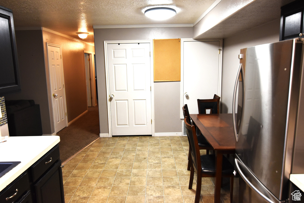 Kitchen with crown molding, light countertops, freestanding refrigerator, a textured ceiling, and dark cabinets