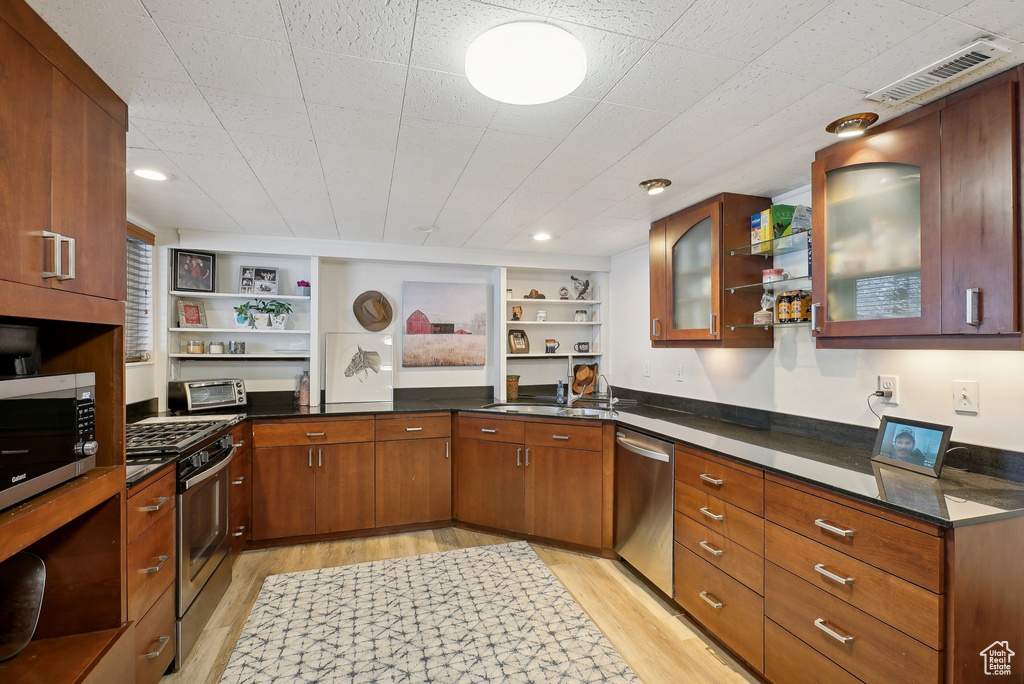 Kitchen with open shelves, appliances with stainless steel finishes, and light wood-style flooring