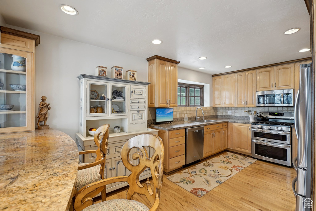 Kitchen featuring stainless steel appliances, a sink, tasteful backsplash, light wood-style flooring, and recessed lighting