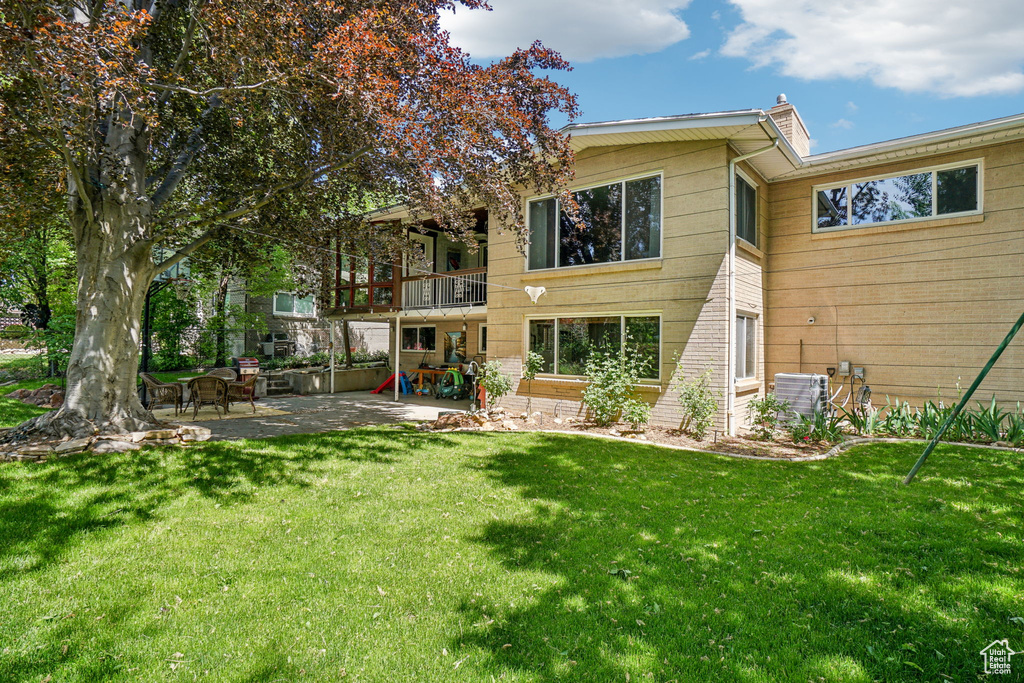 Rear view of property with a patio area, a lawn, a balcony, and central AC