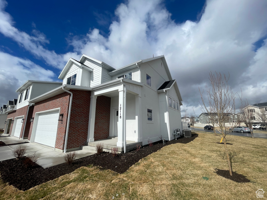 View of home's exterior with brick siding, central AC unit, concrete driveway, covered porch, and a yard
