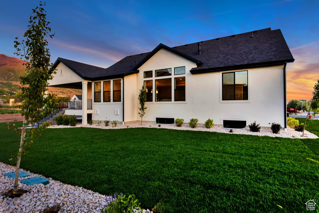 Back of property at dusk featuring a yard, stucco siding, and a shingled roof