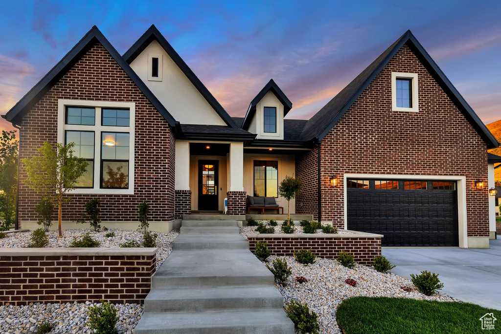 View of front facade featuring brick siding, covered porch, driveway, and stucco siding