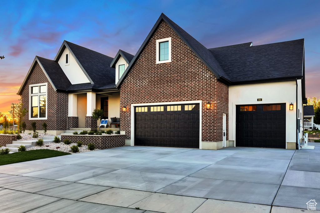 View of front facade featuring a garage, driveway, a shingled roof, brick siding, and stucco siding