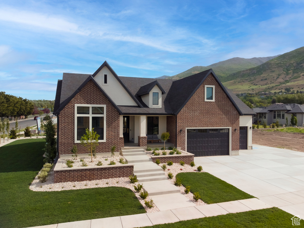 View of front of house with concrete driveway, brick siding, a front yard, covered porch, and a mountain view