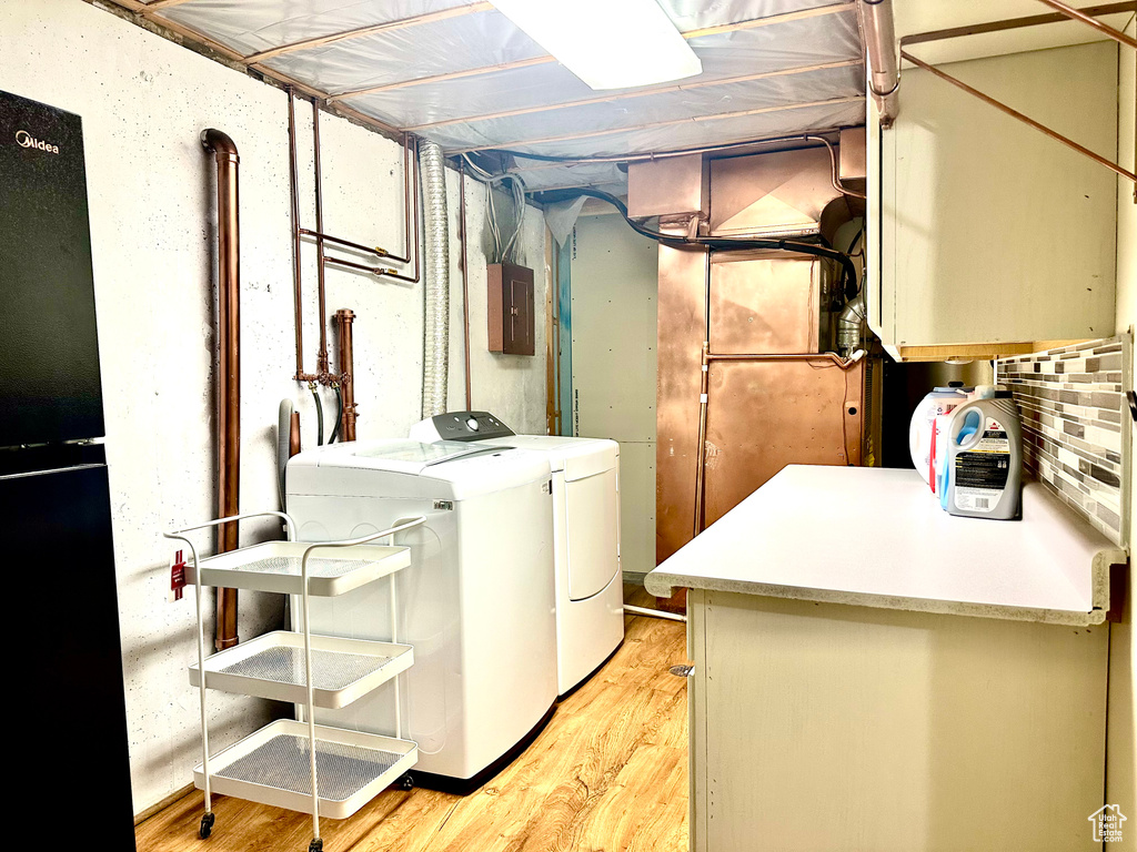 Laundry area featuring separate washer and dryer, cabinet space, electric panel, and light wood-type flooring