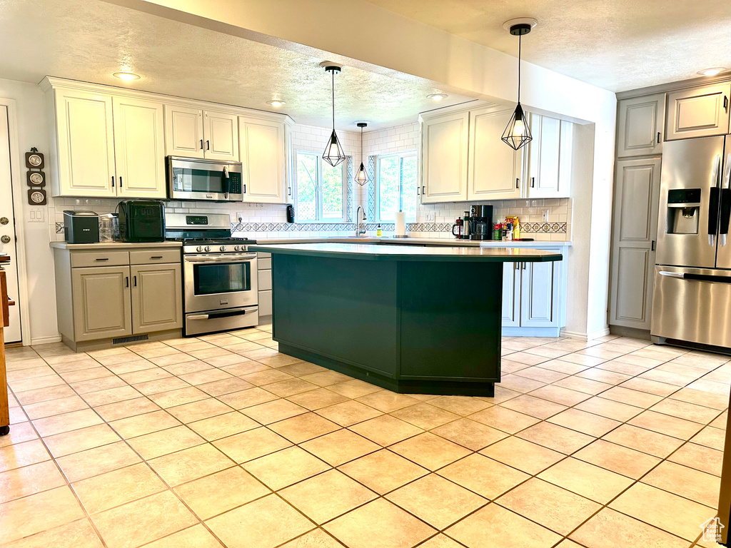 Kitchen featuring stainless steel appliances, a textured ceiling, tasteful backsplash, pendant lighting, and white cabinets