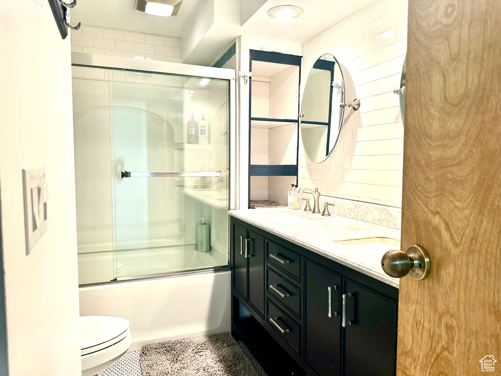 Bathroom featuring double vanity, enclosed tub / shower combo, and toilet
