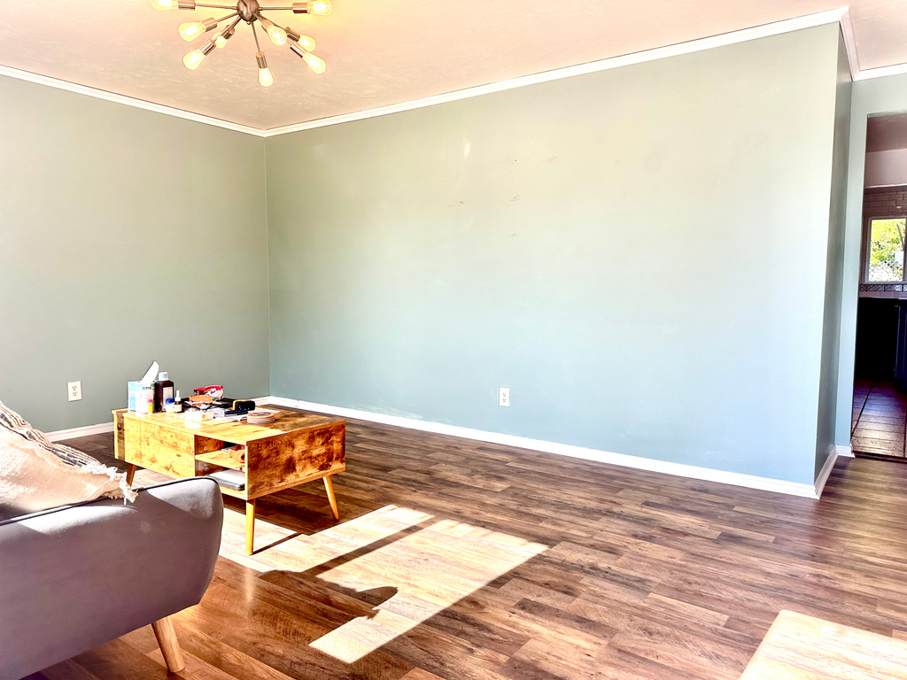 Living room featuring a chandelier, crown molding, baseboards, and wood finished floors