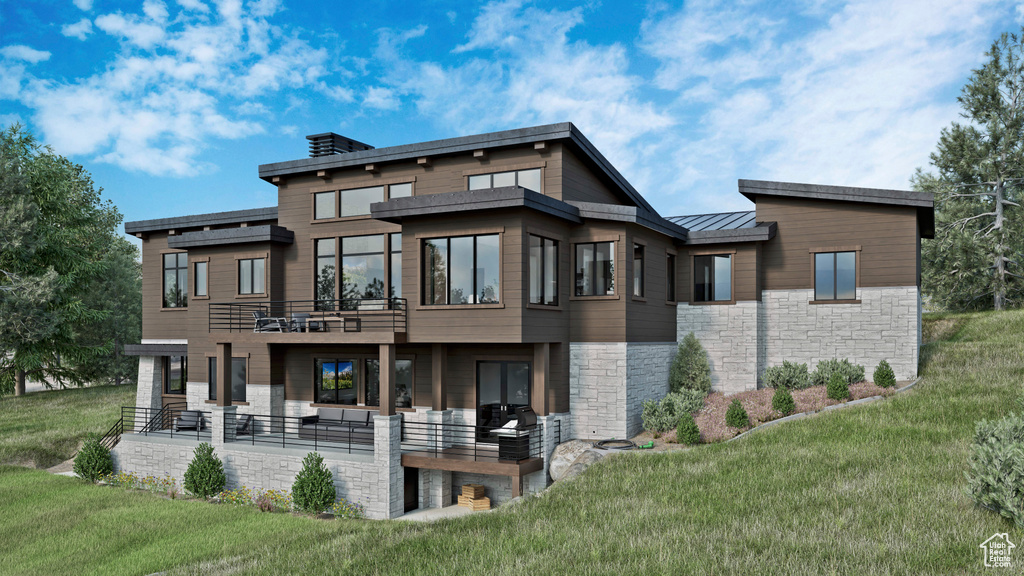 Rear view of house with a yard, a standing seam roof, a balcony, and stone siding