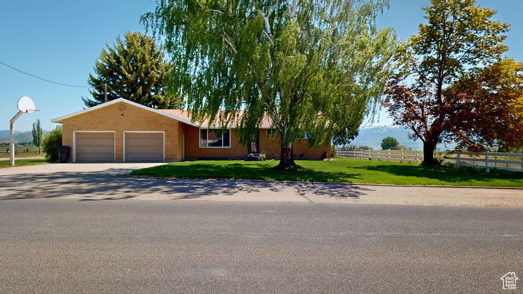 View of front facade with fence, driveway, a front lawn, a garage, and brick siding