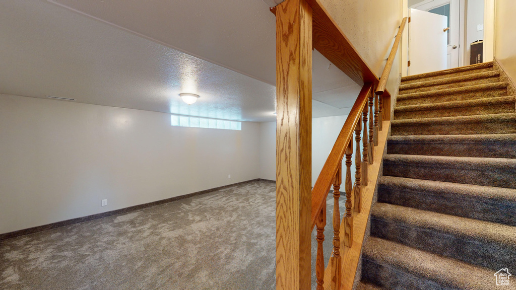 Stairway featuring carpet flooring, visible vents, a textured ceiling, and baseboards