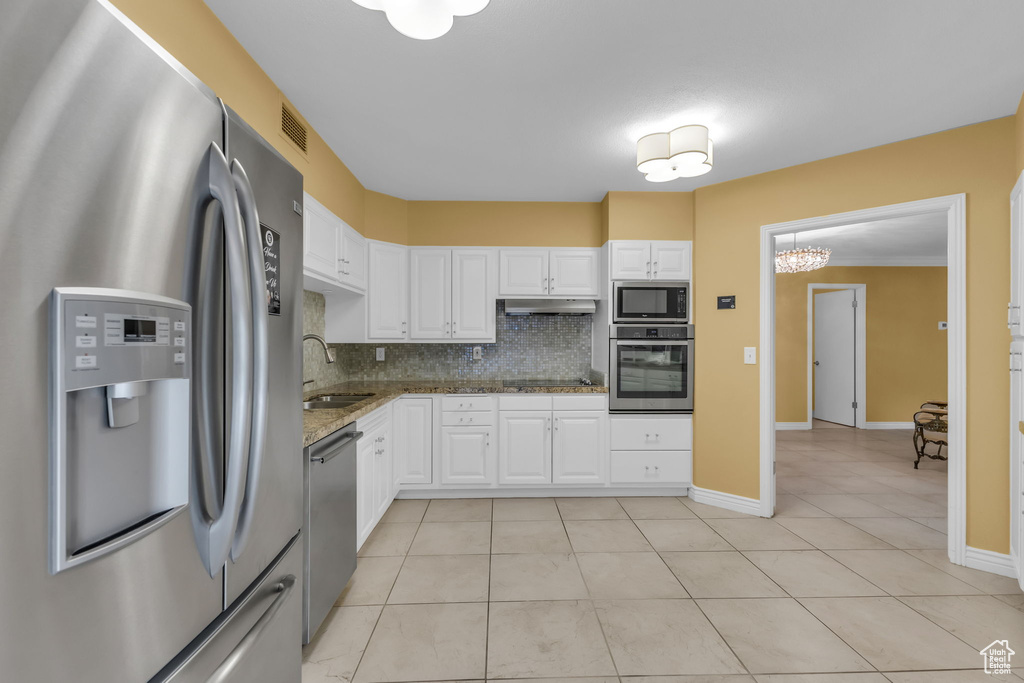 Kitchen with stainless steel appliances, a sink, decorative backsplash, white cabinets, and light tile patterned floors