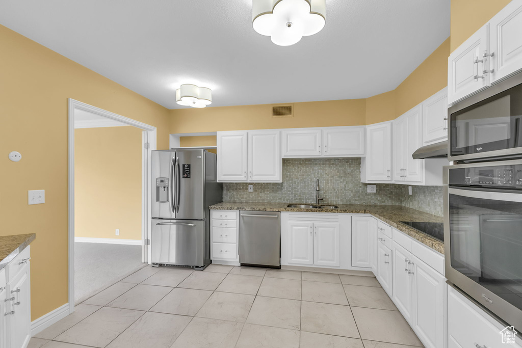 Kitchen with appliances with stainless steel finishes, a sink, white cabinets, decorative backsplash, and baseboards