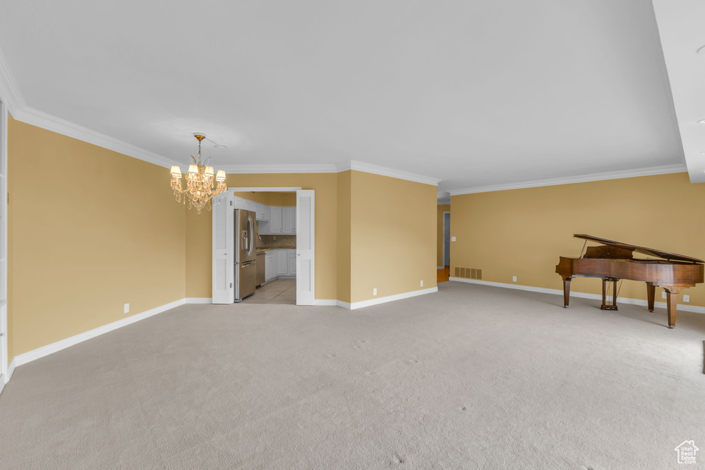 Empty room with a chandelier, ornamental molding, light carpet, and baseboards
