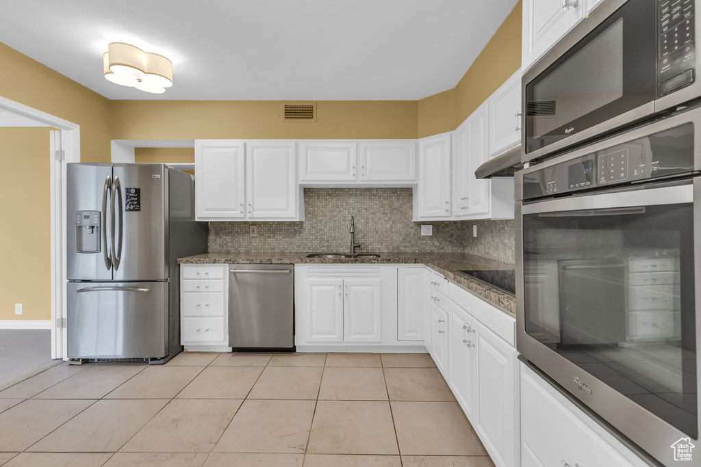 Kitchen with appliances with stainless steel finishes, a sink, white cabinets, backsplash, and light tile patterned flooring