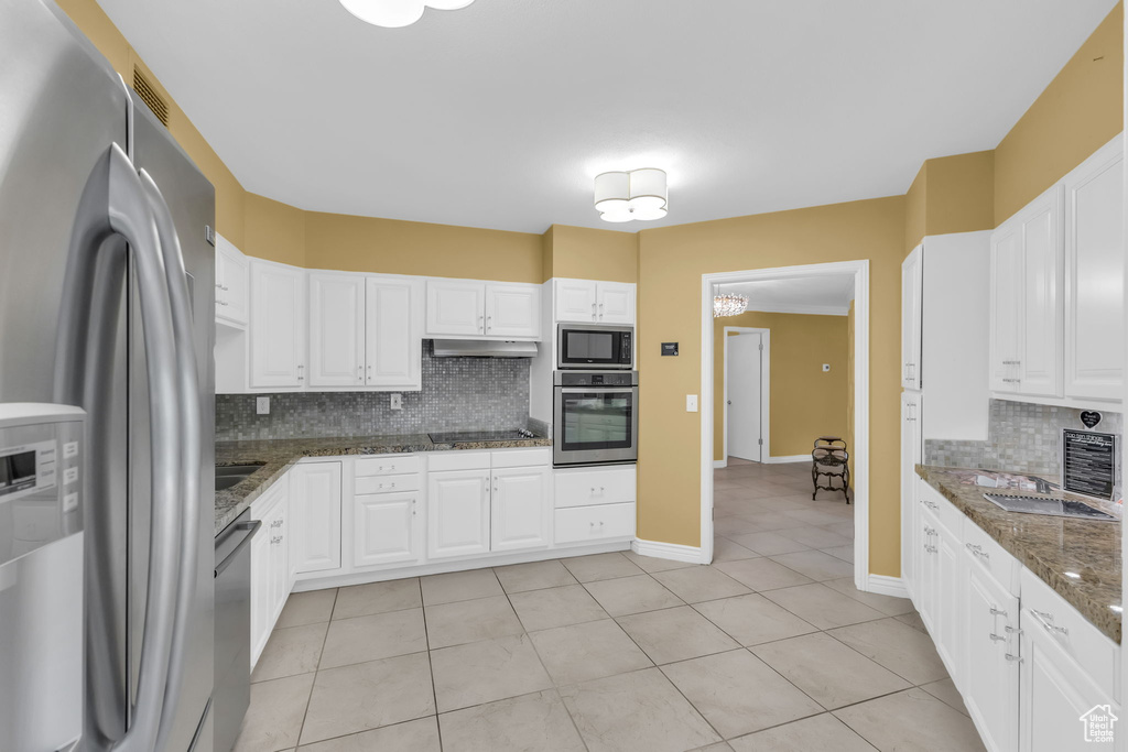 Kitchen featuring stainless steel appliances, under cabinet range hood, backsplash, light tile patterned flooring, and white cabinets