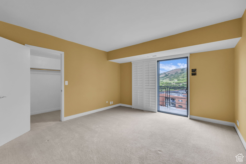 Unfurnished bedroom with access to outside, light colored carpet, baseboards, and a walk in closet
